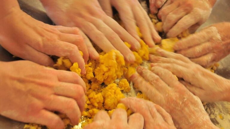 Diverse mani che impastano la pasta fresca a mano per la preparazione dei casoncelli di Solidarietà Covatese.